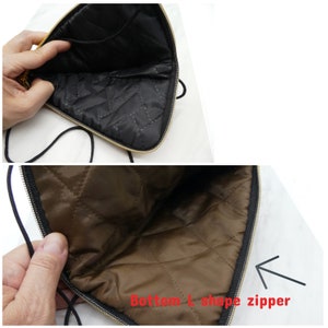 May include: A black quilted pouch with a gold zipper and a black drawstring closure. The zipper is shaped like an L at the bottom of the pouch.