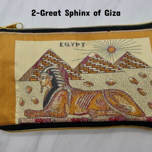 May include: A gold and brown zippered pouch with a black trim. The pouch features an embroidered image of the Great Sphinx of Giza in front of the pyramids. The image also includes the word "EGYPT" and a sun.