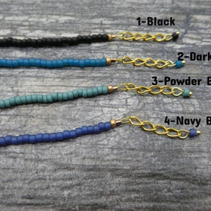 May include: Four strands of beaded necklaces in different shades of blue, black, and aqua. Each strand is attached to a gold chain with a bead at the end. The text "1-Black", "2-Dark Aqua", "3-Powder Blue", and "4-Navy Blue" is written next to each strand.