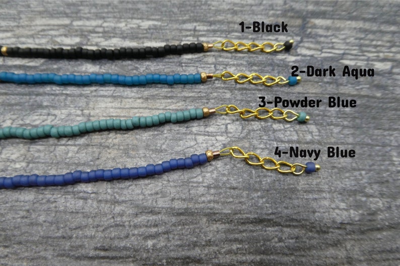 May include: Four strands of beaded necklaces in different shades of blue, black, and aqua. Each strand is attached to a gold chain with a bead at the end. The text "1-Black", "2-Dark Aqua", "3-Powder Blue", and "4-Navy Blue" is written next to each strand.