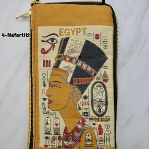 May include: A beige zippered pouch with a gold zipper. The front of the pouch features an embroidered image of Nefertiti, the Egyptian queen, with the word "EGYPT" above her. The image is surrounded by hieroglyphs.