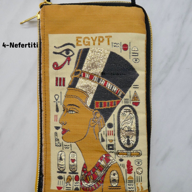 May include: A beige zippered pouch with a gold zipper. The front of the pouch features an embroidered image of Nefertiti, the Egyptian queen, with the word "EGYPT" above her. The image is surrounded by hieroglyphs.