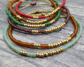 May include: A set of six beaded bracelets with gold accents. The bracelets are layered in a rainbow of colors, including green, brown, red, and light blue.
