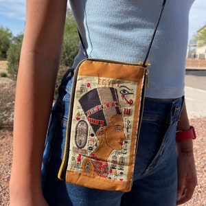 May include: A brown crossbody bag with a zipper closure. The bag features an embroidered image of an Egyptian queen with the word "EGYPT" above her.