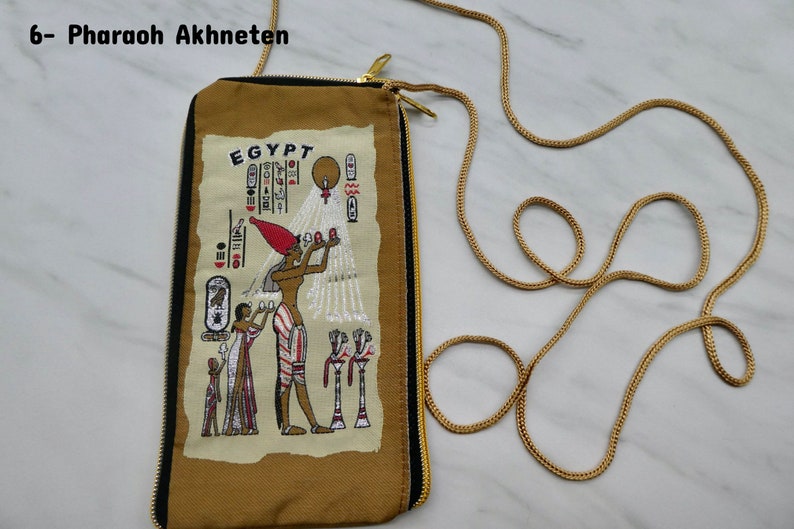 May include: A brown fabric pouch with a zipper closure and a gold chain strap. The pouch features an embroidered image of an Egyptian pharaoh with hieroglyphics and the word "EGYPT".