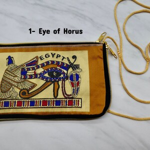 May include: A gold chain purse with a zipper closure. The front of the purse features an embroidered image of the Eye of Horus with the word "EGYPT" above it.