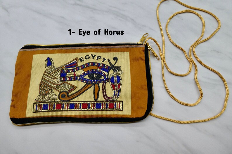 May include: A gold chain purse with a zipper closure. The front of the purse features an embroidered image of the Eye of Horus with the word "EGYPT" above it.