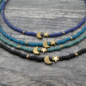 May include: Four layered necklaces with a moon and star charm. The necklaces are black, blue, teal, and purple.