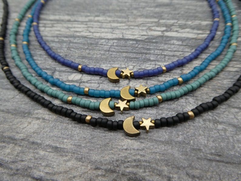 May include: Four layered necklaces with a moon and star charm. The necklaces are black, blue, teal, and purple.