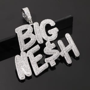Peut inclure: Pendentif argenté avec l'inscription "BIG MESH" en lettres majuscules, incrusté de petites pierres scintillantes. Le symbole du dollar est intégré dans le "S" de "MESH". Le pendentif est doté d'une boucle en haut pour une chaîne.