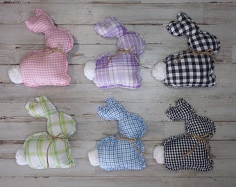 May include: Six plush bunny rabbits in various plaid patterns. The bunnies are pink, purple, black and white, green and white, blue and white, and black. Each bunny has a small white tail.