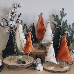 May include: A collection of decorative Christmas tree ornaments in various colors, including white, orange, and green. Each tree is made of a ribbed fabric and has a twine bow at the top. The trees are displayed on wooden bases.