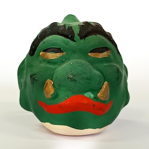 May include: Green ceramic figurine of a monster's face with black eyebrows, gold eyes, and a red mouth.