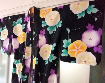 Puede incluir: Yukata negra con un patrón floral de flores moradas, amarillas y blancas sobre un fondo negro. Las flores son estilizadas y se asemejan a las campanillas.
