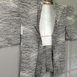 May include: A black and white haori jacket featuring a dense, intricate pattern of fine, swirling lines and small floral motifs. The garment has wide sleeves, an open front, and a contrasting white inner lining with a subtle, faint graphic print.