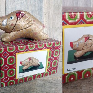 May include: A golden boar figurine with red accents, sitting on a red and green patterned box. The box has the number "824" printed on it. The figurine is also shown in a close-up image on the box.