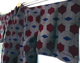 Puede incluir: Un kimono gris con un patrón repetitivo de hexágonos rojos y diamantes azules. El kimono está colgado de una percha de madera. La tela tiene un aspecto texturizado.