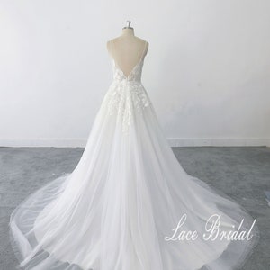 May include: A white wedding dress with a lace bodice and a tulle skirt. The dress has a deep V-neckline and a low back. The dress is on a mannequin and the skirt is flowing out behind it. The text 'Lace Bridal' is visible in the bottom right corner of the image.