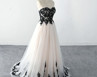 May include: A strapless tulle wedding dress with black lace detailing. The dress has a fitted bodice and a flowing skirt.