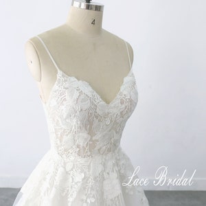 May include: A white lace wedding dress with a sweetheart neckline and spaghetti straps. The dress has a full skirt and is adorned with delicate floral lace. The dress is displayed on a mannequin against a white background. The text 'Lace Bridal' is visible in the bottom right corner of the image.