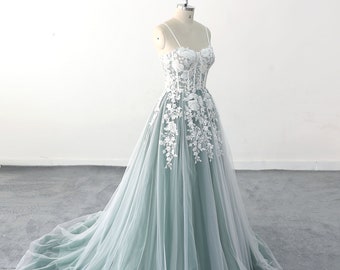May include: A sage green tulle ball gown with white floral lace detailing. The dress has a sweetheart neckline and spaghetti straps.