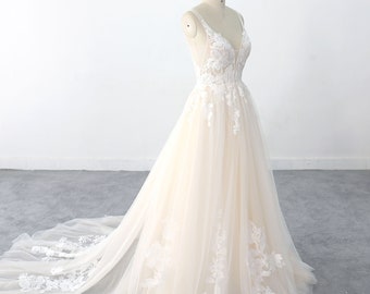 May include: A white lace wedding dress with a V-neckline and a tulle skirt. The dress has a fitted bodice and a flowing skirt. The dress is on a mannequin and has a train. The dress is labeled "Lace Bridal".