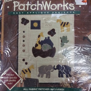May include: A Bucilla PatchWorks Easy Appliqué Project kit featuring a beige fabric with a variety of animal appliqués, including a giraffe, elephant, and zebra. The kit includes all fabric patches, batting, backing, floss, needle, and accessories. The kit is designed by Trice Boerens and has the number 41142.