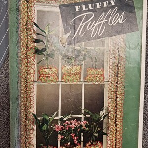 May include: Vintage book cover titled "Fluffy Ruffles" featuring a window with potted plants. The cover has a green border with a red and green lace design. The window has a lace curtain design. The price is 10¢.