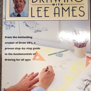 May include: A book cover titled "DRAWING WITH LEE AMES" features a portrait of a man and text. The cover also includes the text "From the bestselling creator of Draw 50's, a proven step-by-step guide to the fundamentals of drawing for all ages."
