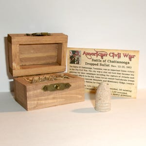 May include: A wooden box with a hinged lid, open to reveal a small compartment filled with straw. A Civil War era bullet stands next to the box, with a card that reads "American Civil War, Battle of Chattanooga, Dropped Bullet."