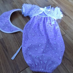 May include: A purple baby gown with a white trim and a white bow. The gown has a small white print of a horse on it. The gown is accompanied by a purple and white bib.