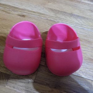 Puede incluir: Un par de zapatos de goma de color rosa brillante con una correa en la parte superior.