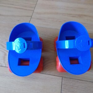 May include: Two blue roller skates with red wheels. Each skate has a blue strap with a star-shaped buckle. The skates are designed for children and are made of plastic.