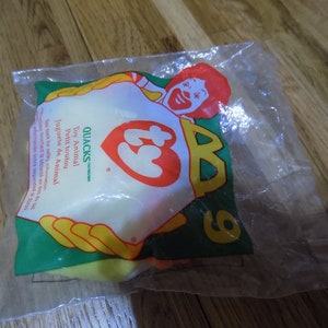 May include: A yellow Ty Beanie Baby plush toy in a clear plastic bag with a red and yellow McDonald's logo. The bag also has the text "QUACKS" and "Toy Animal" printed on it.