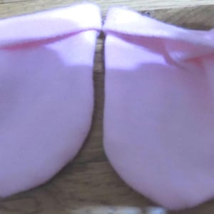 May include: A pair of pink baby booties made of soft fabric. The booties are made of a soft, stretchy material and have a simple design.