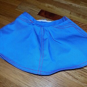 Puede incluir: Una falda azul con costuras rojas alrededor de los bordes. La falda está hecha de una tela suave y ligera.