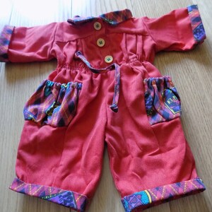 Op de afbeelding: Rode baby-overall met een geruite rand en zakken. De overall heeft een trekkoord in de taille en knoopsluitingen.