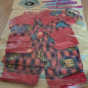 Può includere: Un completo rosso e nero a fantasia per una bambola Cabbage Patch Kids da 40 cm. Il completo comprende una camicia rossa con chiusura a bottoni e un paio di pantaloni con cintura rossa. Il tessuto presenta un motivo a quadri con vari loghi e grafiche Cabbage Patch Kids.