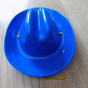 May include: A blue plastic cowboy hat with a yellow string.
