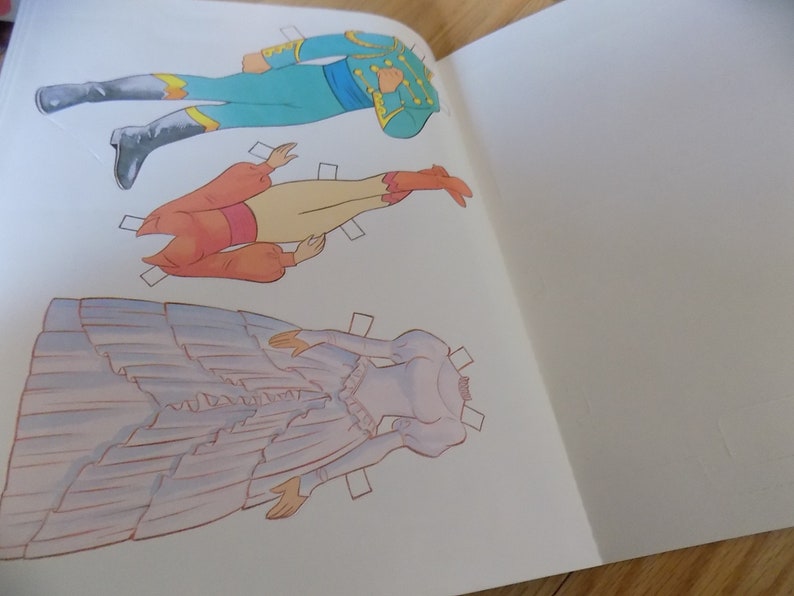 May include: A paper doll set with three figures. The figures are a man in a blue and yellow uniform, a woman in a red and white dress, and a woman in a purple dress. The figures are all cut out and ready to be played with.