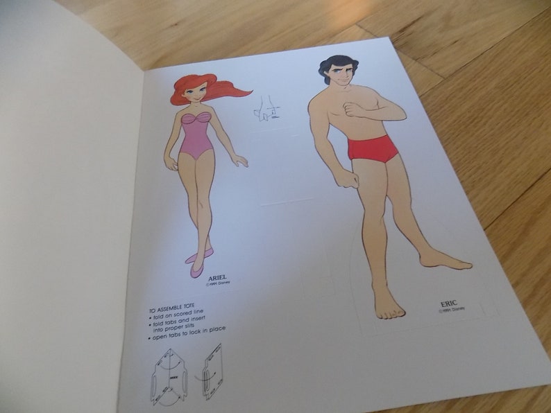 May include: A paper doll set featuring Ariel and Eric from the Disney movie The Little Mermaid. The dolls are printed on white paper and are ready to be cut out and assembled.