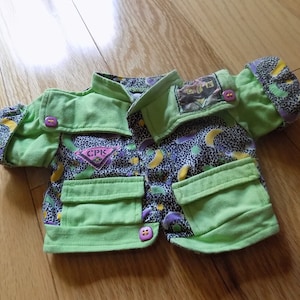 Könnte beinhalten: Eine grüne und violette gemusterte Jacke mit einem CPK-Logo. Die Jacke hat zwei Taschen und einen Knopfverschluss.