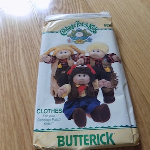 May include: A vintage Cabbage Patch Kids sewing pattern for making clothes. The pattern is for making cowboy outfits for Cabbage Patch Kids dolls. The pattern is from Butterick and has a picture of three dolls wearing the outfits.