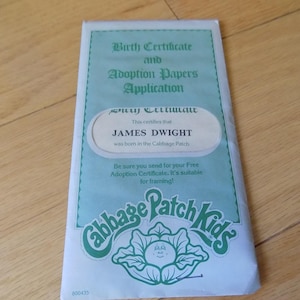 Puede incluir: Un sobre rectangular para documentos de Cabbage Patch Kids en azul claro y verde. El texto dice Birth Certificate and Adoption Papers Application, This certifies that JAMES DWIGHT was born in the Cabbage Patch, y Be sure you send for your Free Adoption Certificate. It's suitable for framing!