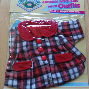 Può includere: Un vestito a quadri rossi e bianchi per Cabbage Patch Kids con rifiniture e bottoni rossi. Il vestito è confezionato in un sacchetto di plastica trasparente con un retro in cartone giallo e bianco. La confezione include il testo "The Official Cabbage Patch Kids Deluxe Outfits" e "Fits All 16" Cabbage Patch Kids."