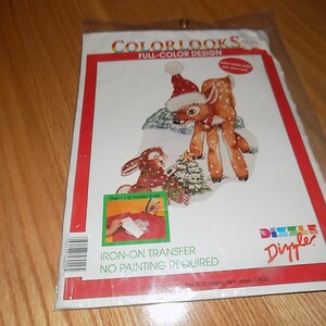 May include: Iron-on transfer design featuring a deer wearing a Santa hat and a rabbit holding a Christmas tree. The design is from Colorlooks and is an iron-on transfer, no painting required. The design is from Dixie.