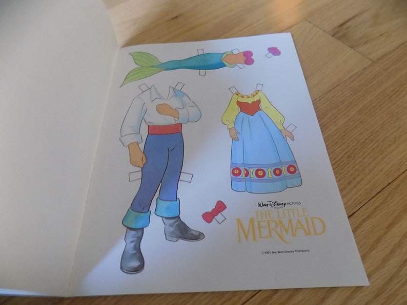 May include: A paper doll set featuring Ariel and Eric from Disney's The Little Mermaid. The set includes Ariel's human form, Eric, and Ariel's tail. The paper dolls are printed on white paper with colorful illustrations.
