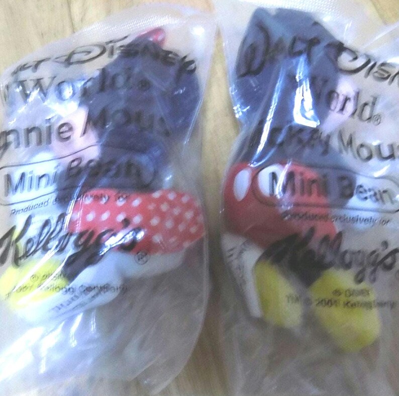 May include: Two plastic bags containing Disney World Mini Bean plush toys. One bag features Minnie Mouse with red and white polka dot shorts and the other features Mickey Mouse with yellow shorts. Both bags have the Kellogg's logo and text that reads "Disney World's Minnie Mouse Mini Bean" and "Disney World's Mickey Mouse Mini Bean".