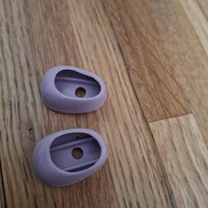 Pode incluir: Duas pontas de silicone para fones de ouvido de cor roxa. As pontas são de forma oval com um pequeno furo no centro.