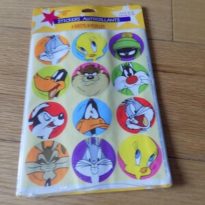 May include: A package of stickers featuring cartoon characters. The stickers are round and colorful, with images of Bugs Bunny, Daffy Duck, Tweety Bird, and other Looney Tunes characters. The package has text that reads "Stickers Autocollants 4 Sheets/4 Feuilles."